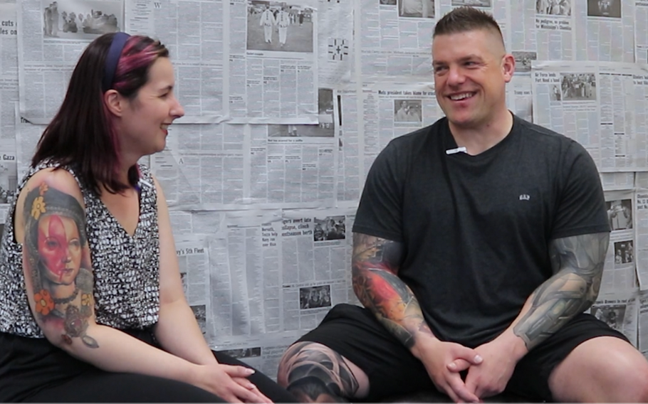 Interviewer and Adam Black laughing and chatting for interview against a background of newspapers